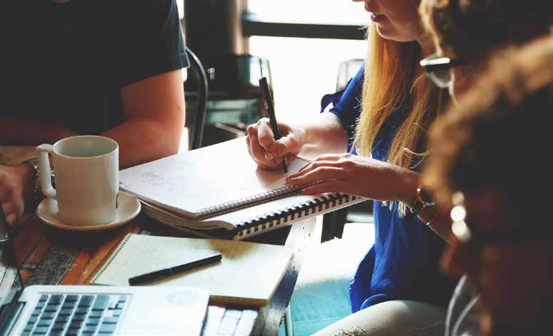 Personas trabajando juntas en una mesa con ordenador y cuadernos